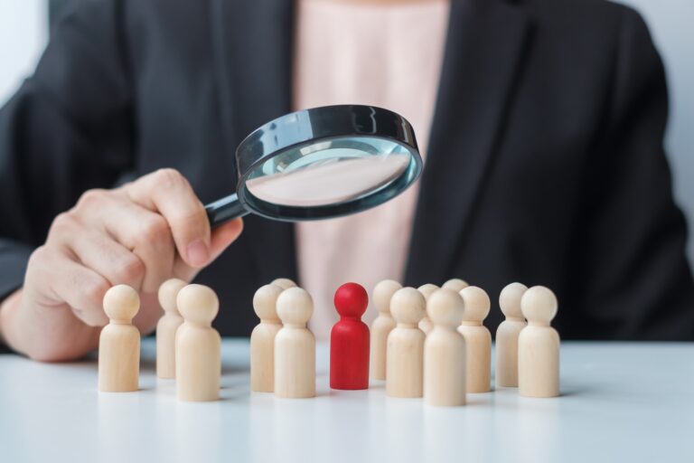 Businesswoman hand holding magnifying glass for recruiting leader man wooden from crowd of employees