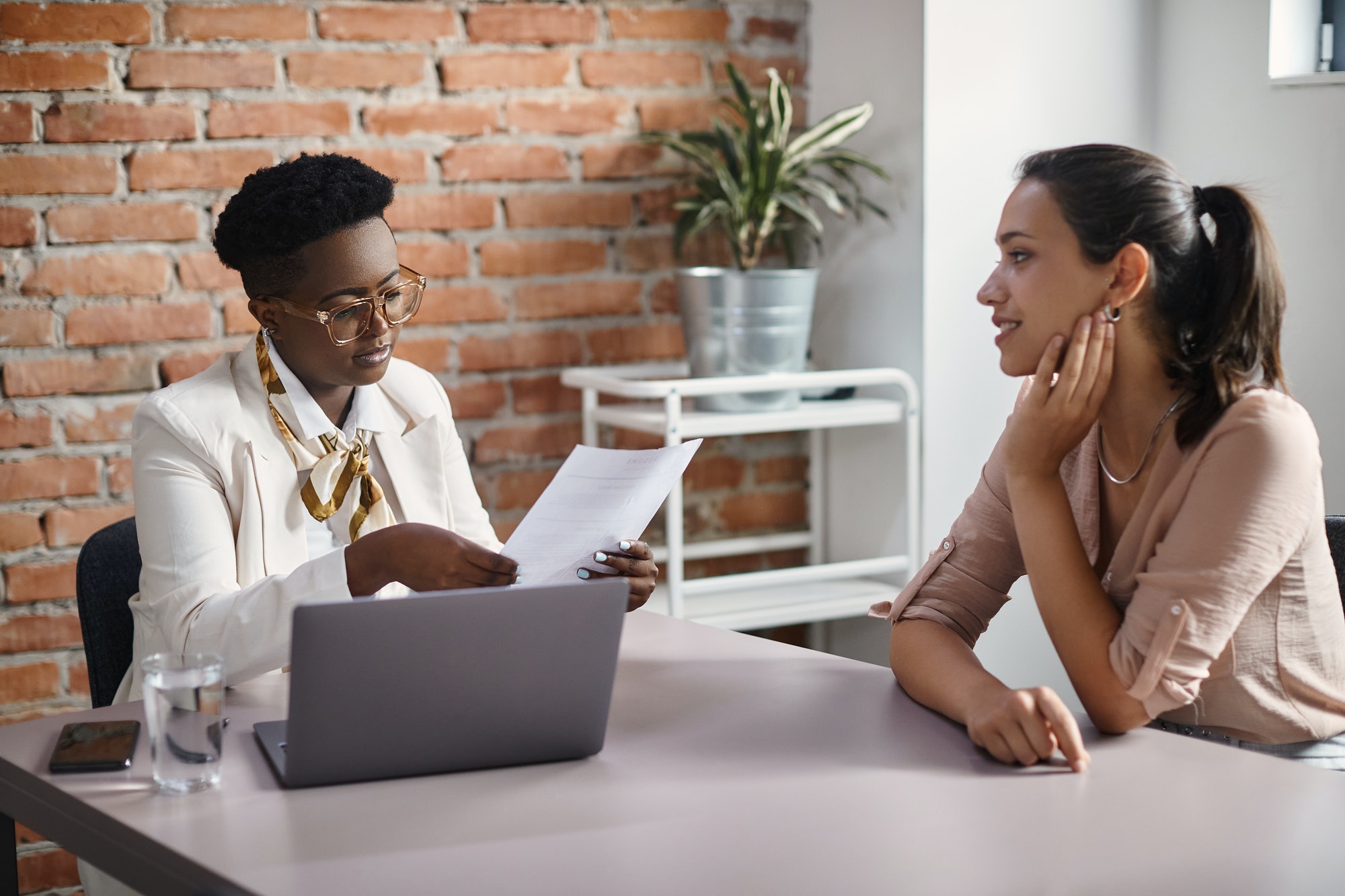 Black businesswoman reading resume of female candidate during job interview in the office.
